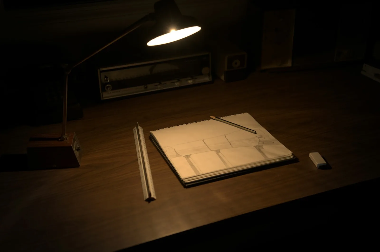 A desk with a sketchbook, pencils and an eraser under a lamp