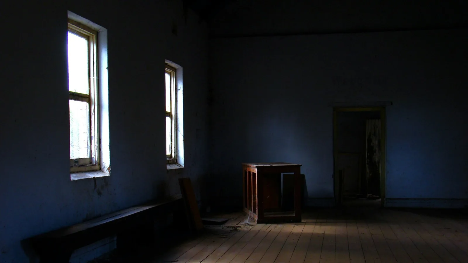 A dark, empty room with two tall windows, the only light coming through them